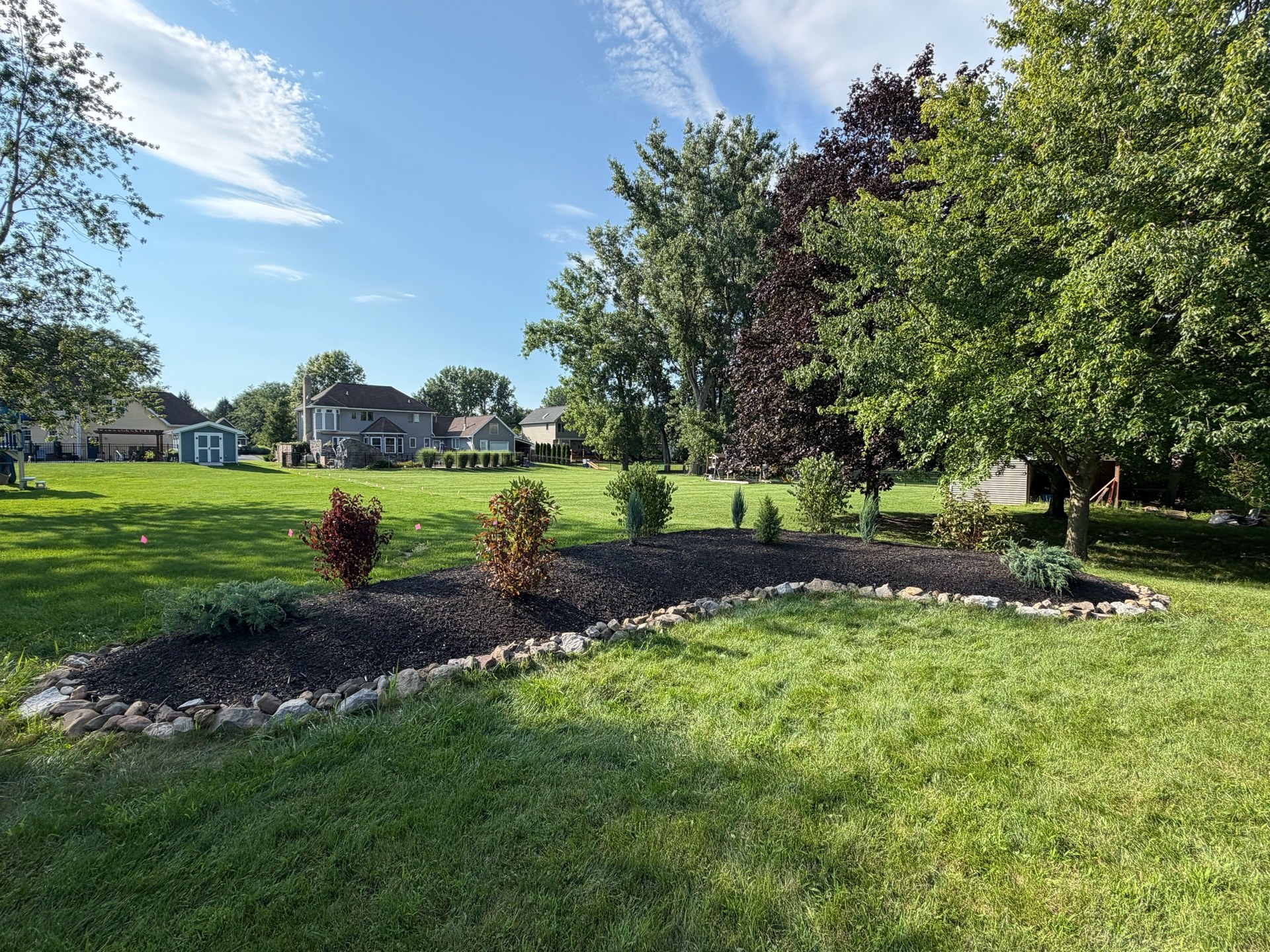 Garden bed rebuilt from an overgrown mound — machine-leveled, landscape fabric, reset boulder ring and fresh mulch (Photo 3)