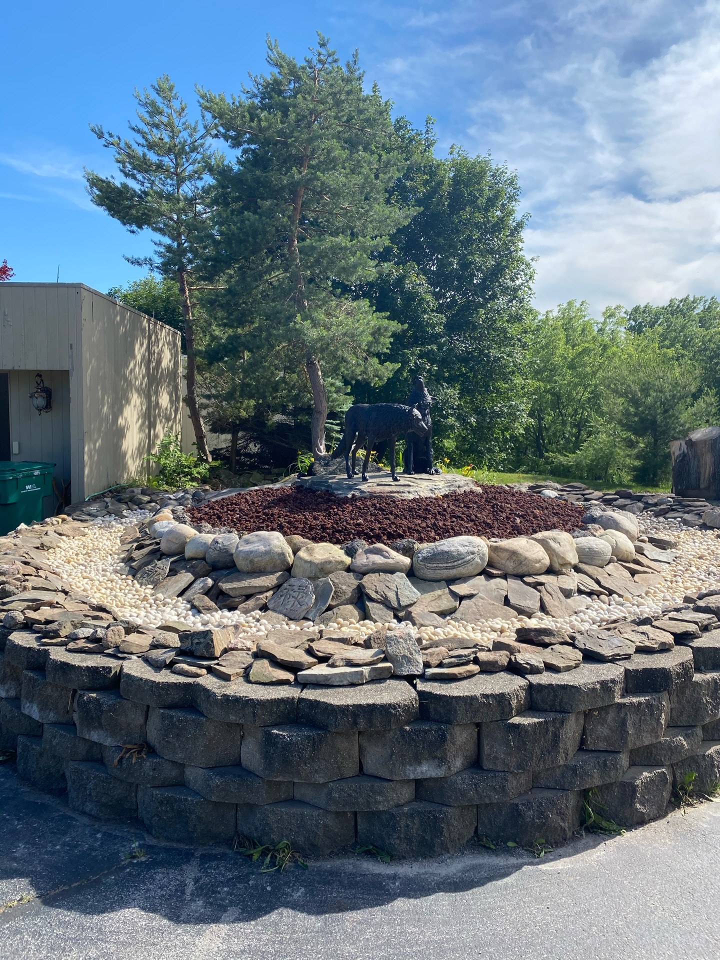 Finished stone feature bed with wolf statues, new stone rings and fresh mulch after a complete tear-out and redesign